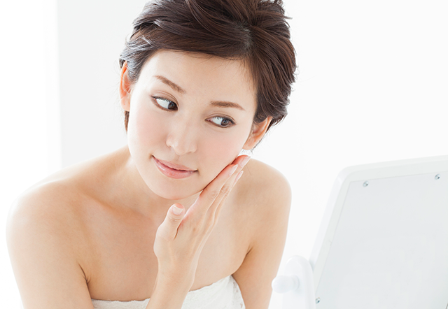 鏡で頬を見る女性